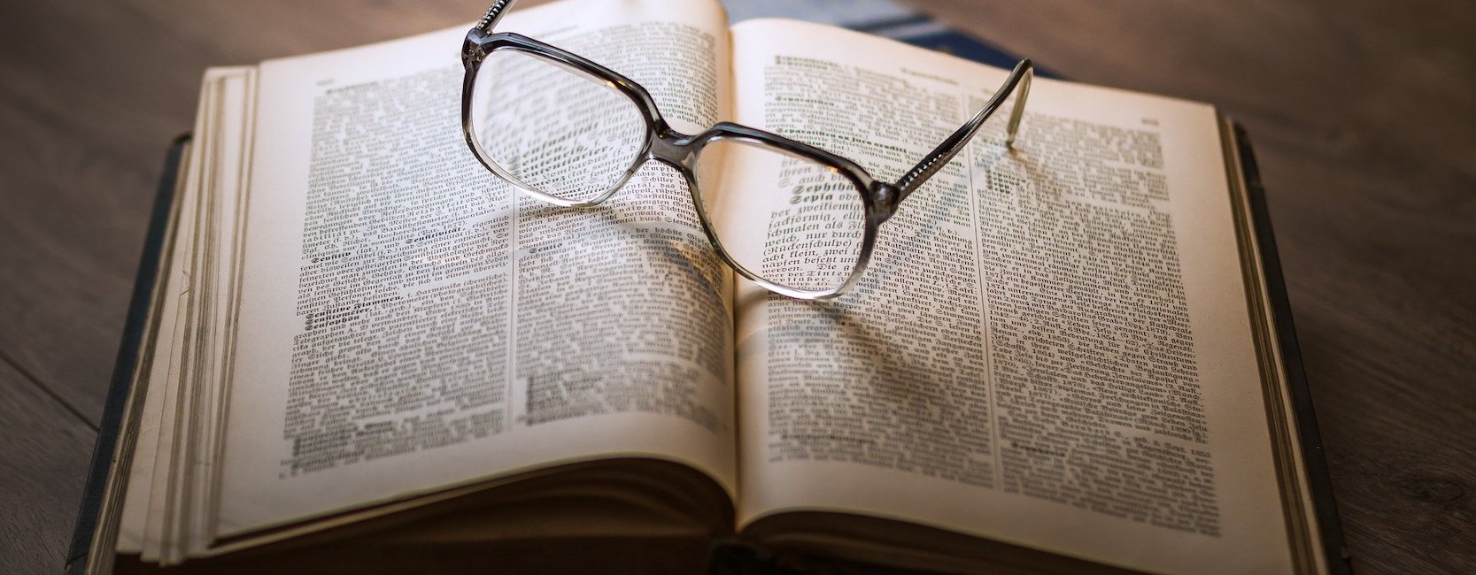 Symbolbild eines geöffneten Buches mit einer Brille darauf